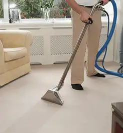 Professional carpet cleaner using a hot-water extraction wand and hose machine in a living room in San Antonio, TX.