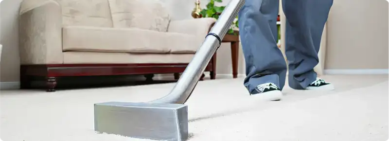 Carpet cleaning technician using a hot-water extraction wand on a light-colored carpet in a living room, San Antonio, TX.