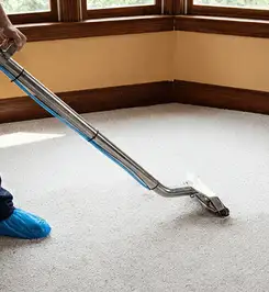 Steam carpet cleaning technician using a hot-water extraction wand on a residential carpet, wearing blue protective shoe covers San Antonio, TX.