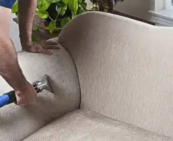 Professional upholstery cleaner deep-cleaning a fabric sofa with a handheld extraction tool and hose in San Antonio, TX.